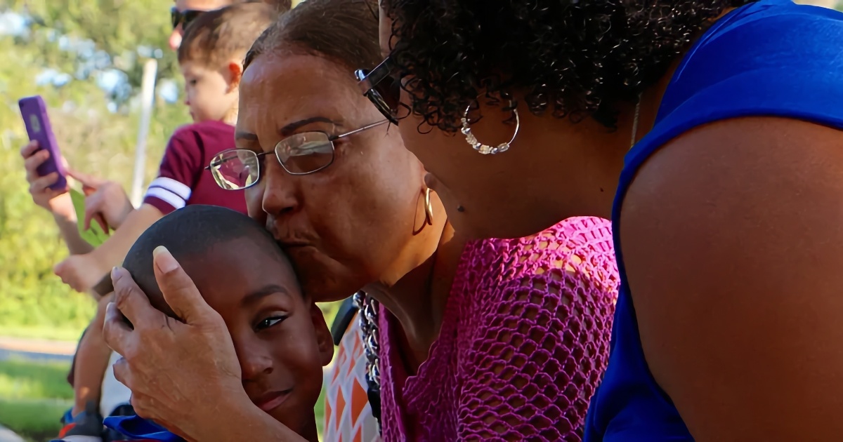 Black woman kissing a black child at school with another Black woman looking on