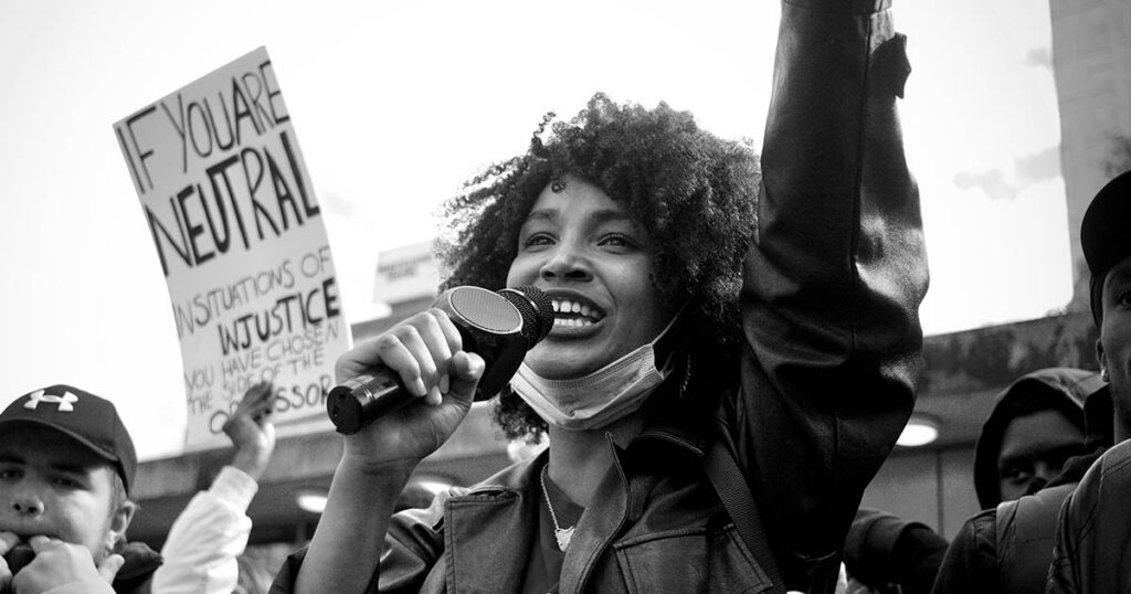 A young woman smiles while holding a microphone at a protest.