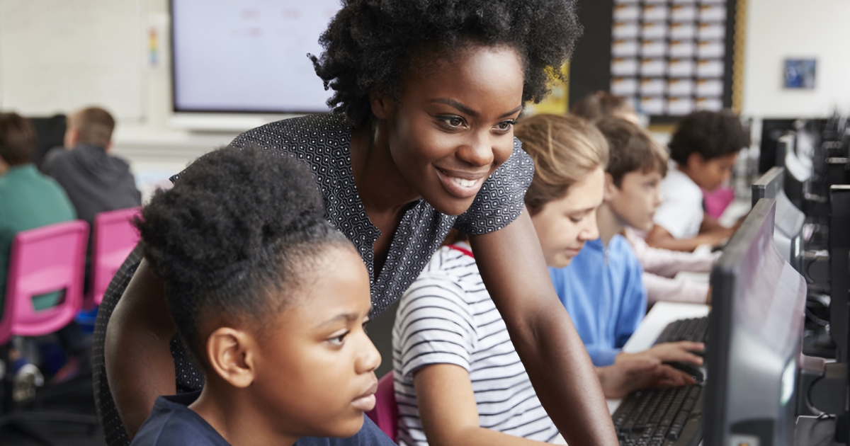 Black teacher leaning over a black student's shoulder in a school computer lab