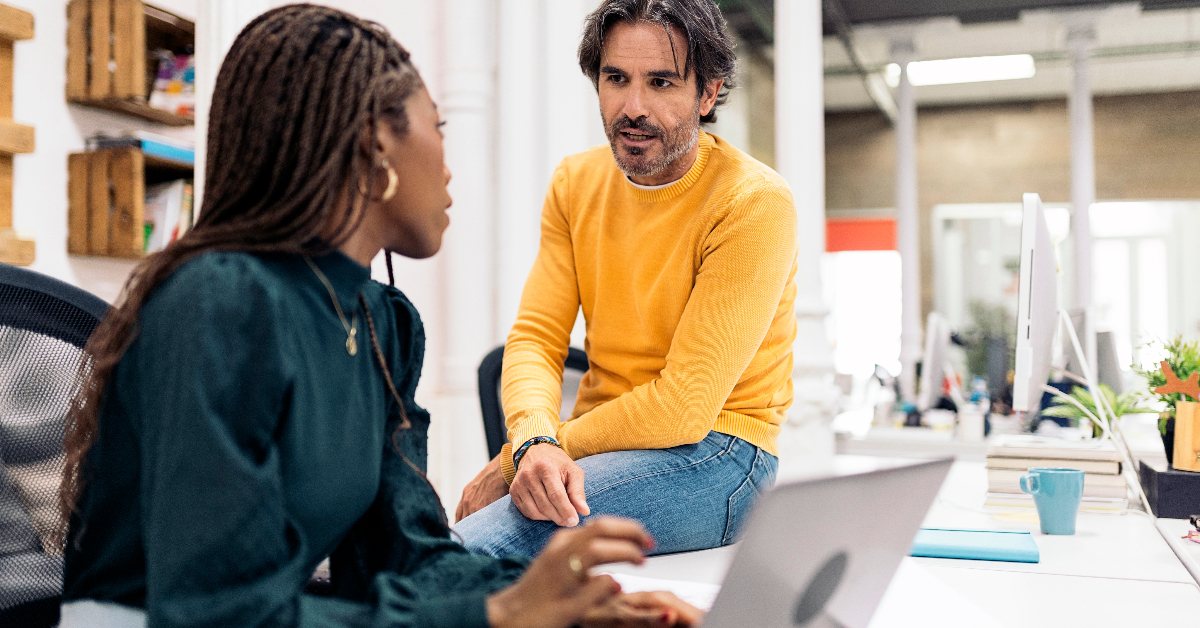 Adult business man working with his african coworker and talking. They are using a laptop.