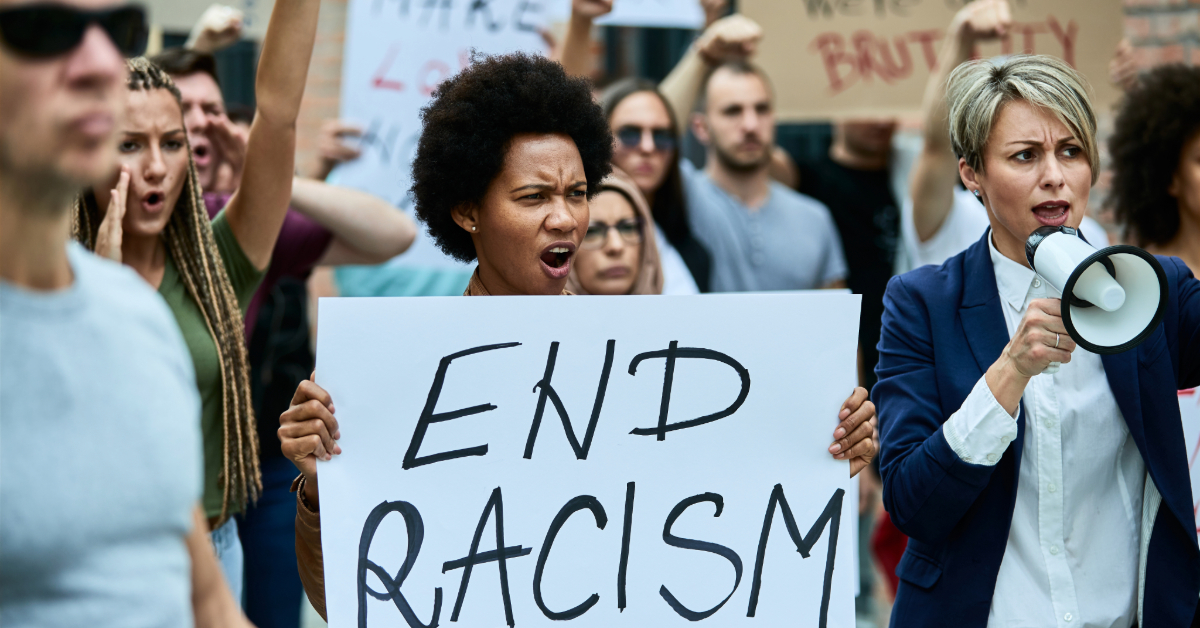 Crowd of people protesting against racism on the streets. Focus is on African American woman holding banner with End racism inscription.
