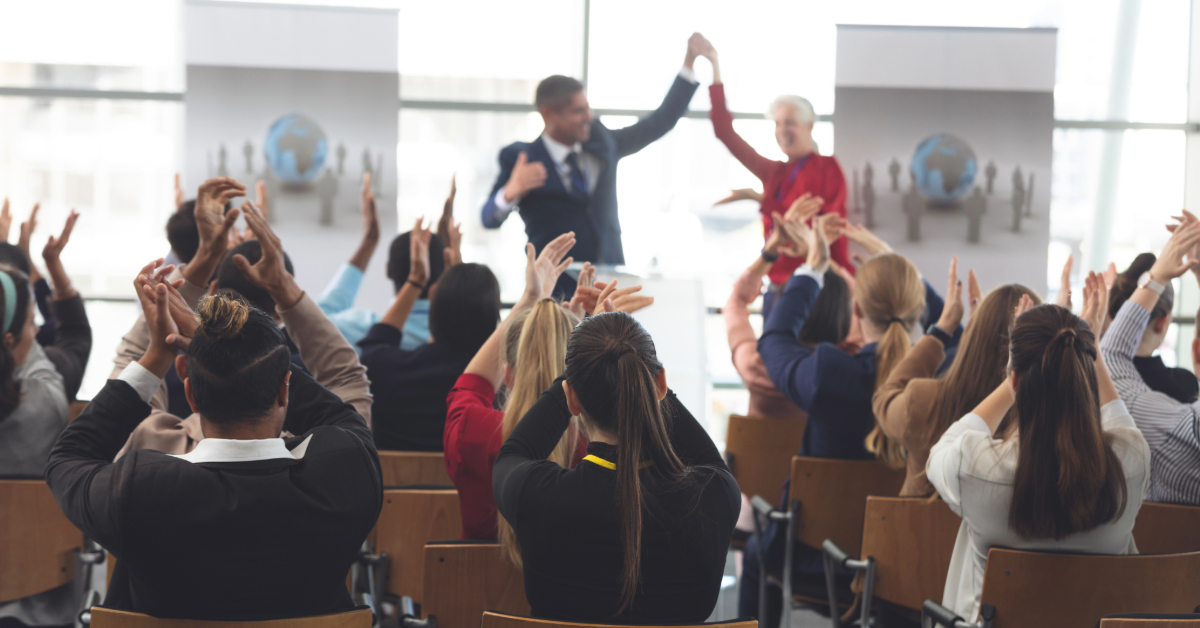 Rear view of diverse business people applauding and celebrating while they are sitting in front of multi-ethnic business executives at business seminar in office building