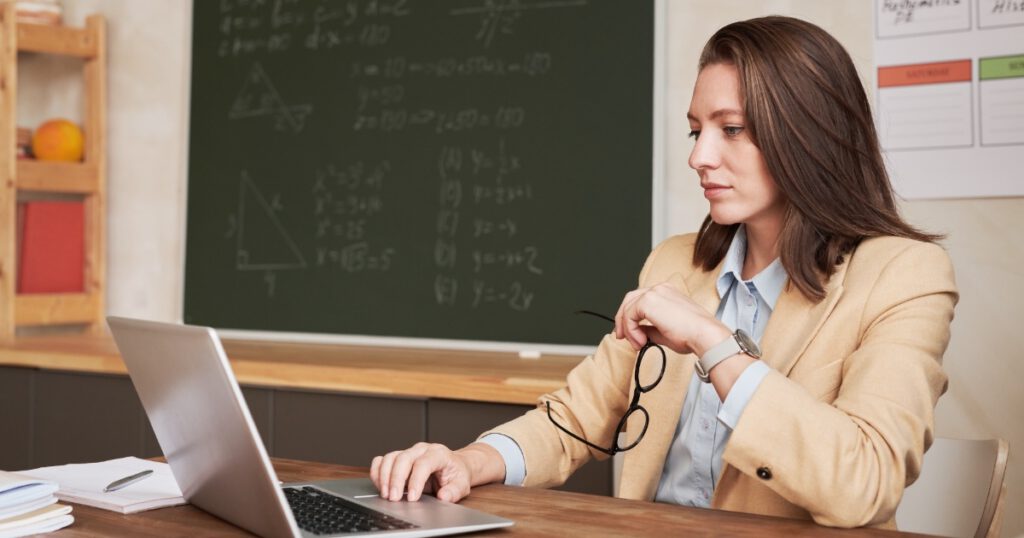 White Woman Teacher Working at Desk in Classroom