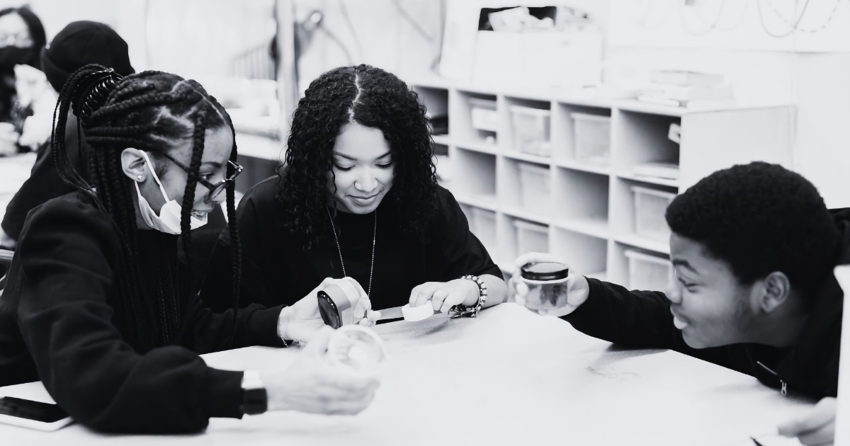 Black and white image of a Black woman teacher working in a classroom with two Black students