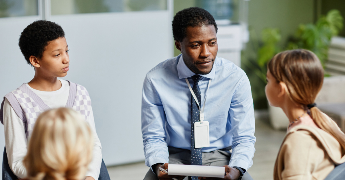 Portrait of young African-American psychologist listening to children in support group circle