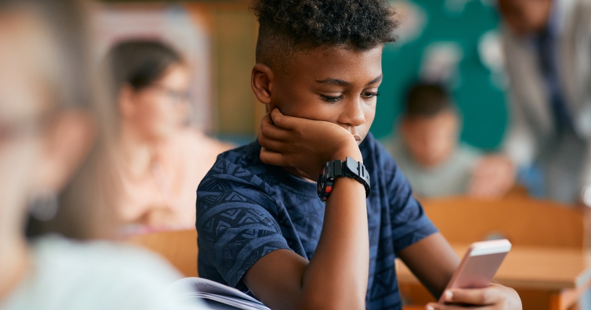 Black elementary student typing text message on smart phone in the classroom.