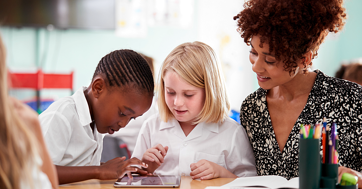 A young boy and a young girl looking at their schoolwork with a teacher looking over them.
